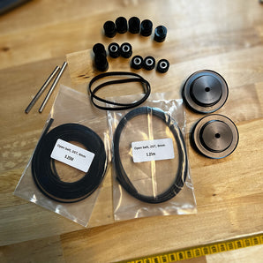 LH Stinger motion kit with Gates 2GT open and closed-loop belts, black Runice pulleys and idlers, bearings, and metal shafts on a workbench.