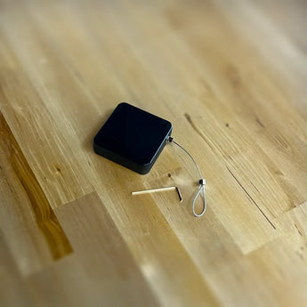 Black 500g retractable tool tether with plastic housing, steel cable loop, and hex key for Stealth Press mounting