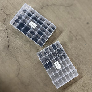 Two clear grid boxes holding black nickel LH Stinger fastener kit screws, washers, nuts, T-nuts, inserts, and shims.